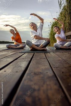 three people sitting on the ground doing yoga exercises in front of water and bamboo trees