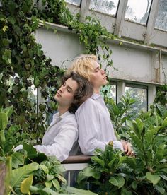 two people are sitting on a bench surrounded by plants and greenery in a greenhouse