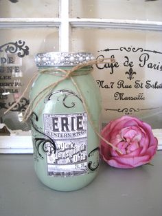 a pink flower sitting on top of a table next to a jar with writing on it