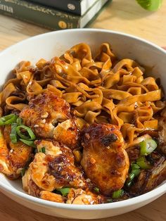 a white bowl filled with pasta and meat on top of a wooden table next to a stack of books