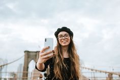 a woman taking a selfie with her cell phone in front of the brooklyn bridge