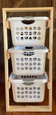 three plastic laundry baskets stacked on top of each other in a wooden storage rack against a wall