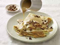 a white plate topped with pancakes covered in caramel sauce and pecans next to a cup of coffee