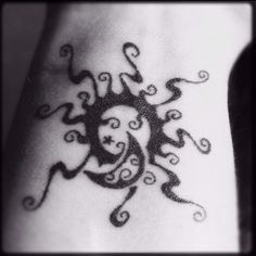 a black and white photo of a sun tattoo on the wrist with swirls around it