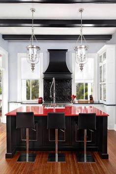 a kitchen with black cabinets and red counter tops, white walls and hardwood flooring