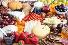 an assortment of cheeses, fruits and crackers on a cutting board