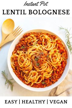 a white bowl filled with spaghetti and meat on top of a table next to a wooden spoon