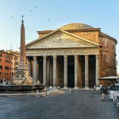 people are sitting at tables in front of an old building with columns and a fountain