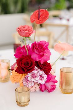 flowers and candles on a white table with pink, red and orange flowers in vases