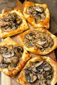 several small pizzas with mushrooms on them sitting on a cutting board