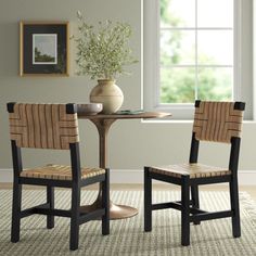 two chairs sitting at a table in front of a window with a vase on it