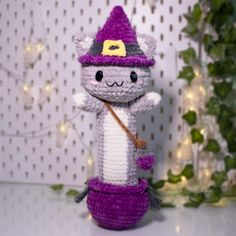 a crocheted cat with a broom on top of a table next to a christmas tree