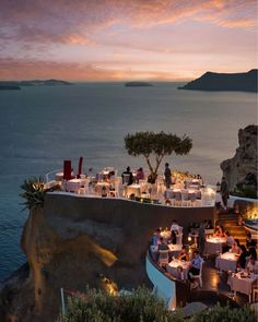 an outdoor dining area overlooking the ocean at dusk with people sitting around tables and eating