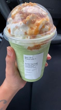 a person holding up a cup of ice cream and toppings in their hand while sitting in a car