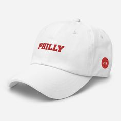 "Philly Embroidered Dad Hat with Red Text, Red and white Philly hat, Philadelphia hat, Philly ball cap, Cute Philly Hat An outfit paired with a dad hat just hits differently. A truly classic item that serves a fresh look any time of the day. * 100% chino cotton twill * Green Camo color is 35% chino cotton twill, 65% polyester * Unstructured, 6-panel, low-profile * 6 embroidered eyelets * 3 ⅛\" (7.6 cm) crown * Adjustable strap with antique buckle * Blank product sourced from Vietnam or Bangladesh This product is made especially for you as soon as you place an order, which is why it takes us a bit longer to deliver it to you. Making products on demand instead of in bulk helps reduce overproduction, so thank you for making thoughtful purchasing decisions!" White Snapback Visor Hat With Letter Print, White Letter Print Visor Snapback Hat, White Letter Print Snapback Visor Hat, Classic Red Hat With Curved Bill, Classic Red Curved Bill Hat, Classic White Snapback Hat With Visor, Classic Red Dad Hat With Curved Brim, White Letter Print Dad Hat For Baseball Season, White Fitted Hat With Embroidered Logo For Sports Events