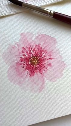 a pink flower painted on white paper next to a brush