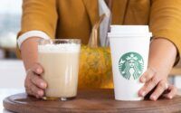 two people holding starbucks cups on a table