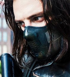 a man with long hair wearing a black mask and leather jacket, looking at the camera