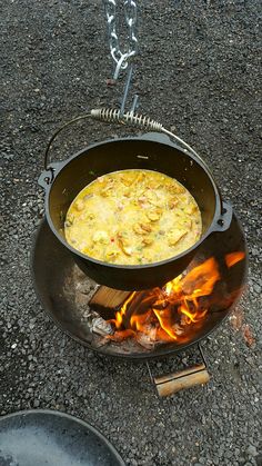 a large pot filled with food sitting on top of a fire pit next to a frying pan