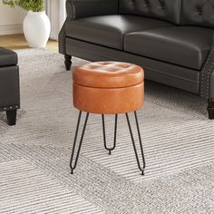 a brown ottoman sitting on top of a rug next to a black couch and chair