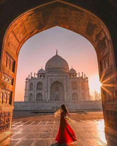 a woman in a long red dress is walking through an archway towards the tajwaf