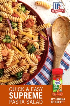 a pasta salad with tomatoes, broccoli and cheese in a red bowl next to a wooden spoon