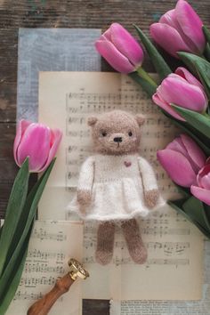 a teddy bear in a white dress next to pink tulips and sheet music