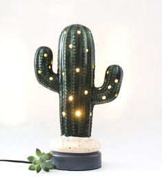 a green cactus with lights on it sitting next to a small plant and a white wall