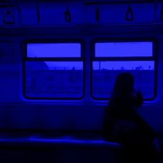 a person sitting on a subway train looking out the window at night, with blue lighting