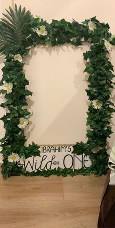 a photo frame made out of fake flowers and greenery on the side of a wall