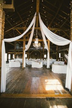 the inside of a barn decorated with white linens and chandelier draped over tables