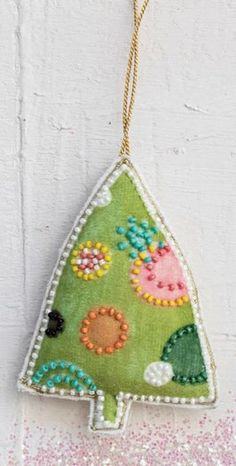 a christmas tree ornament hanging from a string on a white wall with pink and green glitters