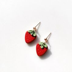 two red strawberry shaped earrings with green leaves hanging from the ear wires on a white surface