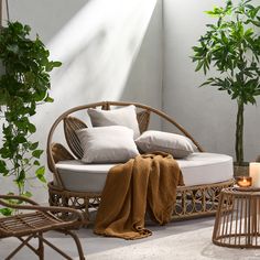 a wicker couch with pillows on it next to a table and potted plant