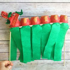 a hand holding a toothpick with green paper and red decorations on it, in front of a wooden background