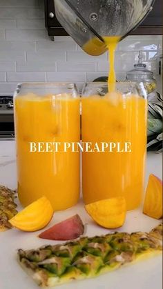 two glasses filled with orange juice sitting on top of a white counter next to sliced fruit