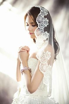 a woman wearing a wedding veil and holding her hands together