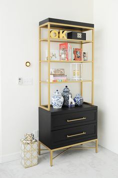 a black and gold bookcase with two drawers on it, next to a white wall