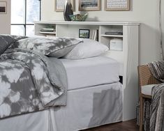 a bed with white sheets and pillows in a bedroom next to a chair, bookshelf and pictures on the wall