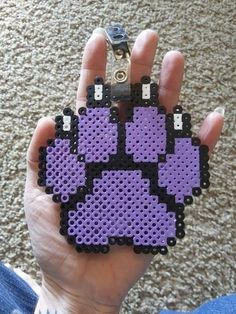 a hand holding a purple and black piece of art made out of perler beads