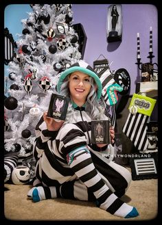 a woman sitting in front of a christmas tree holding two mugs and a cell phone