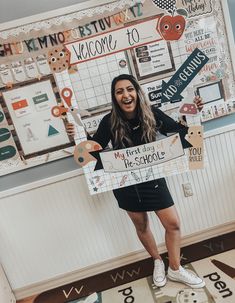 a woman standing in front of a bulletin board holding a sign that says welcome to my first day of the school