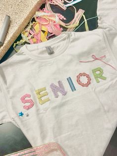 cute unique dior inspired senior shirts with ribbon stars multicolor colorful aesthetic 2024 senior shirt inspiration diy make your own graduating shirts friends matching senior shirt ideas new senior shirt ideas micheals crafts ribbon cute coquette senior t Shirt senior shirts 2024 senior shirt ideas 2024 trendy tiktok aesthetic senior shirts 2006 senior shirt designs things to do for seniors senior bucket list senior friend group highschool bucket list simplistic minimalistic creative senior shirts with the word senior and decorations viral trending Senior Shirts Ideas High School, Matching Senior Shirts, Senior Year Clothes, Senior Shirts Aesthetic, Senior Year Of High School Outfits, Senior Shirts Ideas 2025 Diy, Senior Ideas Shirt, Aesthetic Senior Shirts, Senior Stuff Ideas