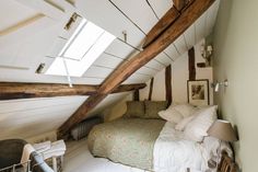 an attic bedroom with white walls and exposed wood beams on the ceiling, along with a bed