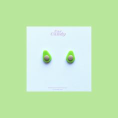 two avocado shaped earrings sitting on top of a green surface with the words ear candy