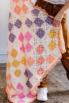 a woman is holding up a crocheted blanket