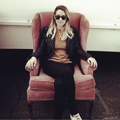 a woman sitting in a pink chair with her legs crossed and wearing black sunglasses,