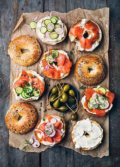 an assortment of bagels and sandwiches on a piece of wax paper with cucumbers