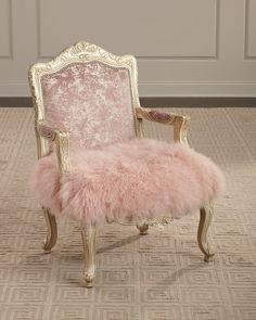 an old chair with pink fur on the seat and gold trimmings, in front of a white paneled wall