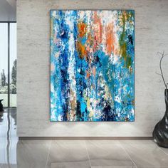 an abstract painting hangs on the wall next to a vase